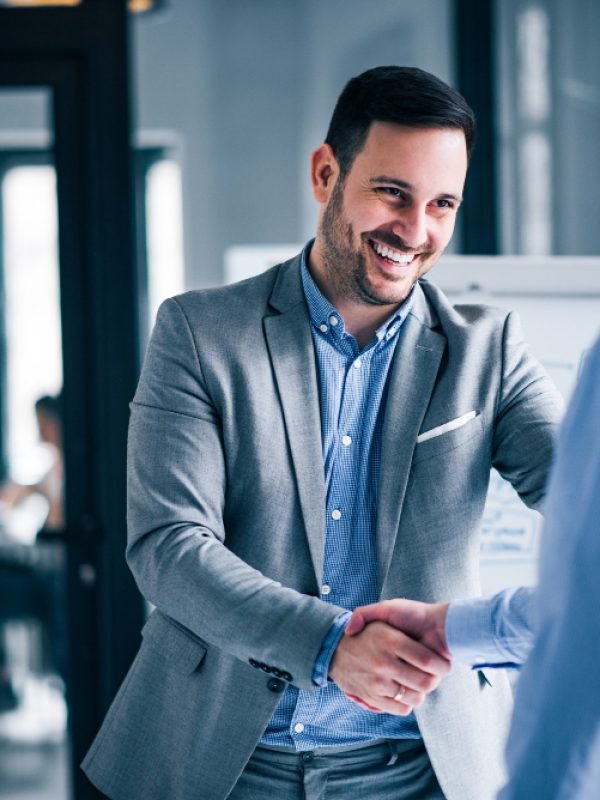 two-smiling-businessmen-shaking-hands-while-standing-office